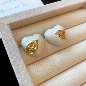 Detail von 18k vergoldeten Herzohrringen mit weißer Emaille und goldenem Blatt.
