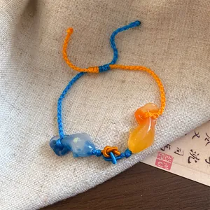 Detailopname van een geweven koi-visarmband in Chinese stijl met blauwe en oranje bedels