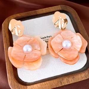 Macro view of elegant pearl and peach acrylic flower earrings with creased gold metal