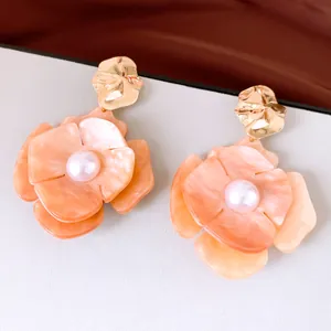 Detailed macro of peach acrylic flower stud earrings with center pearls and gold studs.