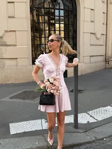 Elegant blonde model in pink puff sleeve lace mini dress holding a rose bouquet outdoors