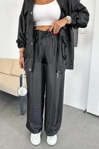 Dettaglio completo di un completo nero a due pezzi con giacca a tasche e pantaloni ampi.