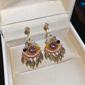 Detail shot of bohemian stud earrings with purple crystal and teardrop tassels.