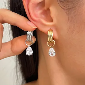 Gros plan de créoles dorées et argentées avec pendentifs en zircone poire sur l'oreille
