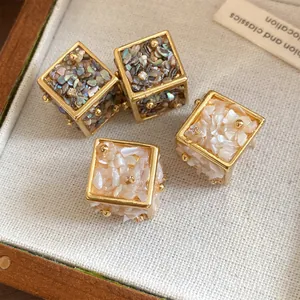 Détail des boucles d'oreilles cubes géométriques 3D avec fragments de nacre et or