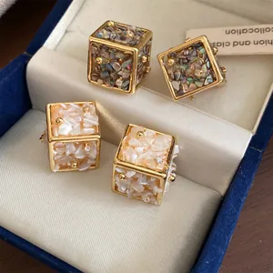 Vue détaillée de boucles d'oreilles cube avec incrustations de nacre et petits cristaux.