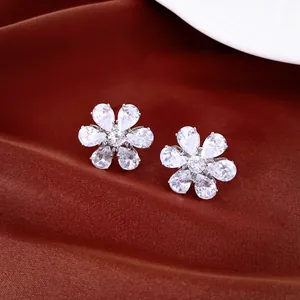 Detalle de pendientes de botón de flor con circonitas brillantes sobre tela rojiza.