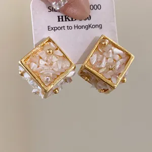 Vue détaillée des boucles d'oreilles géométriques dorées avec incrustation de nacre blanche.
