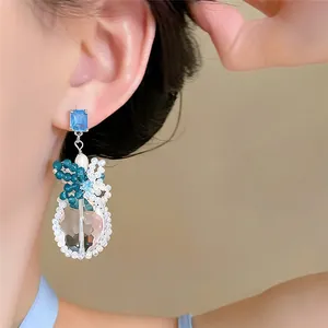 Primo piano di orecchini pendenti in cristallo con perno blu e decori floreali sull'orecchio