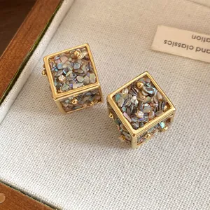 Détail macro de boucles d'oreilles cubes dorées élégantes avec éclats de nacre colorés.