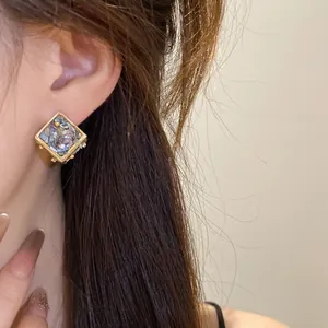 Gros plan détaillé d'une boucle d'oreille losange géométrique avec incrustation de nacre irisee.