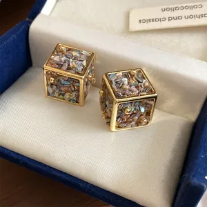 Gros plan de boucles d'oreilles cubes dorées avec incrustation de nacre dans un écrin.