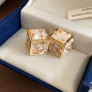 Gros plan de boucles d'oreilles cubes avec incrustation de nacre et monture dorée.
