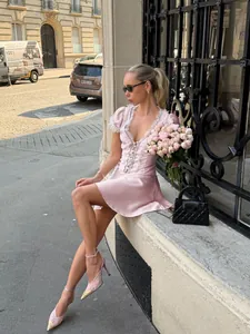 Model wears a light pink French style lace mini dress with puff sleeves on a city street.