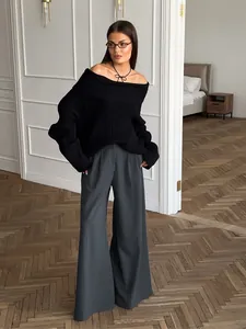 Elegantes Modell in schwarzem schulterfreiem Pullover und grauer weiter Faltenhose im Büro
