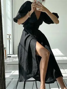 Side view detail of a black puff sleeve dress with a high slit and tie-waist design.