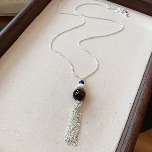 Dettaglio di un'elegante collana con nappa, perla di vetro marrone e catena in argento