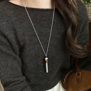 Dettaglio di una collana lunga con nappe e perle di vetro su un maglione marrone scuro