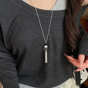 Primo piano di una lunga collana con nappa elegante, sfera di vetro e perla su maglione grigio.