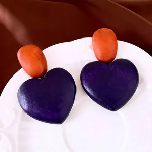 Vintage purple heart-shaped wooden drop earrings with orange stud on a decorative white plate.