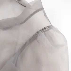 Detailansicht der zarten gerafften Schulternaht an einer grauen, transparenten Netzbluse.