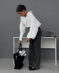 Modell in weißem drapiertem Polo-Hemd und Weitbein-Jeans in minimalistischem Büro-Ambiente