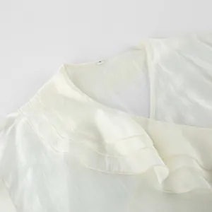 Close-up of elegant cream tencel wrap top with layered ruffle collar detail.