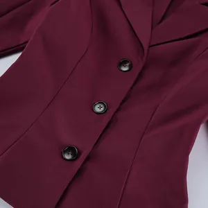 Primo piano di un blazer sciancrato bordeaux da donna con tre bottoni neri decorativi.