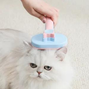 Ergonomic pink and blue oval pet deshedding brush used on a fluffy white cat for grooming