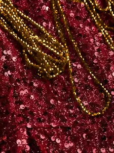 Detailed macro view showing sparkling dark red sequins and gold chain on evening gown