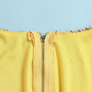 Detailed macro view of the metal zipper and gold sequins on a yellow bodycon party dress