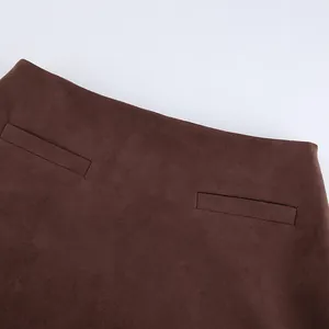 Close-up of brown suede skirt texture showing detailed welt pockets and high waist.