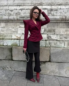 Dettaglio di un blazer rosso scuro con spalline a punta e pantaloni neri a zampa d'elefante.