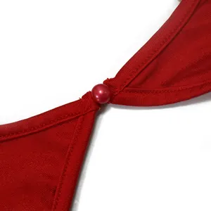 Détail d'une robe longue rouge montrant une boucle en perle décorative sur tissu texturé.