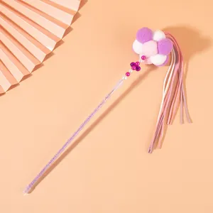 Detail view of fairy cat wand toy with purple pompoms and long tassels on orange background