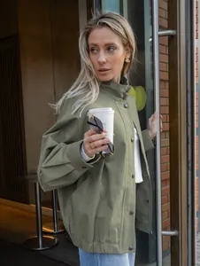 Moderne vrouw in een groene cargo-jas buiten met een stijlvolle koffiebeker in haar hand