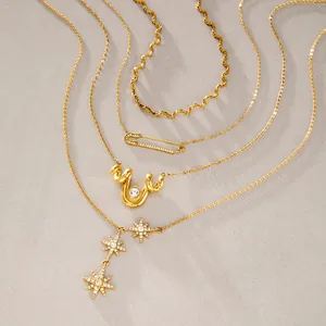 Vue détaillée de colliers superposés en acier titane doré avec pendentifs étoile et épingle.