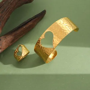 Vue détaillée d'un ensemble bracelet martelé doré et bague cœur sur surface verte