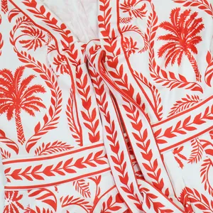 Vue détaillée du motif palmier rouge et du nœud frontal sur le tissu blanc de la combi