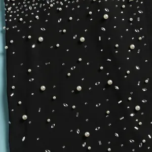 Dettaglio in primo piano del tessuto nero della tuta con perle e strass scintillanti
