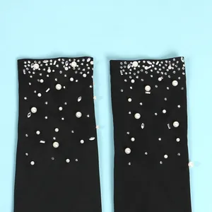 Dettaglio di eleganti perle e strass su tessuto nero di tuta attillata.