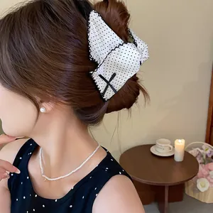 Detail view of a large white polka-dot bow hair claw clip styled on a brown bun.