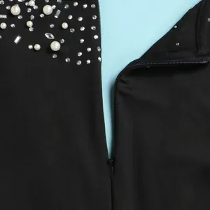 Primo piano dettagliato di una tuta nera con perle decorative, strass e cerniera lampo.