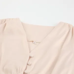 Detail van elegante abrikooskleurige satijnen jurk met V-hals en beklede knopen