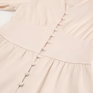 Detail van een roze satijnen jurk met beklede knopen en geplooide taille-afwerking