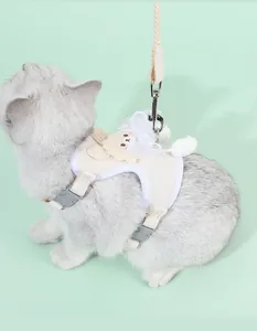 Dettaglio di una pettorina per gatti beige con decorazione a forma di orso e fiocco.