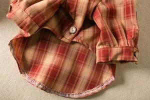 Close-up detail of a brown plaid pet shirt showing buttons and stitching.