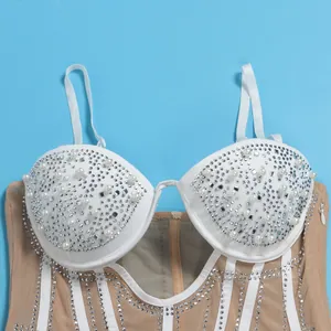 Close-up of white corset cups adorned with pearls and rhinestones on mesh camisole dress.