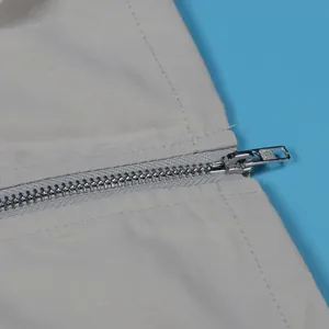 Close-up of durable silver metal zipper detail on light gray cargo skirt fabric.