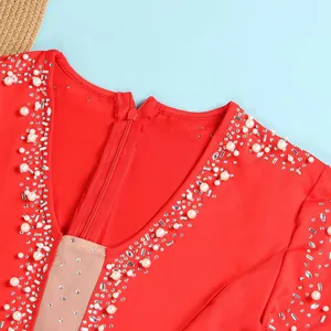 Dettaglio di una tuta rossa con scollo a V decorata con perle bianche e strass scintillanti
